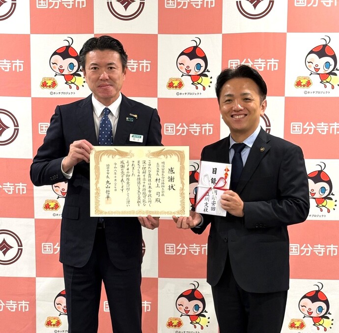 「私の地元応援募金」贈呈式にて、パネル前で市長と明治安田生命保険相互会社の立川支社長が撮影した写真